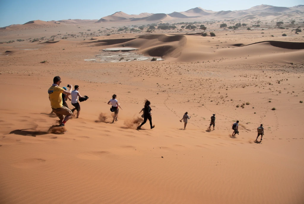 Travelers running down a red sand dune in the Namibian desert