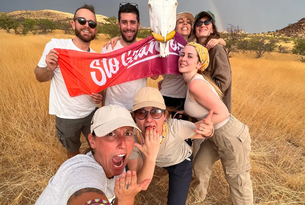 Group selfie in the savanna with the Sto Gran Tour banner and an animal skull found along the way