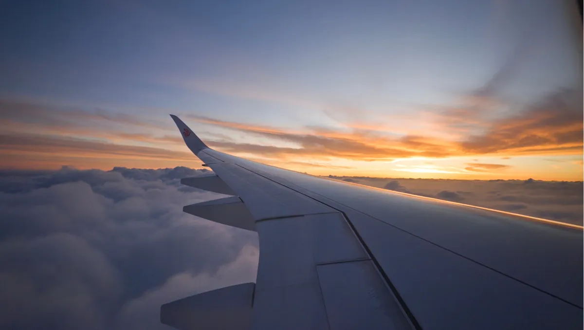 The plane's wing above the clouds, with the sun setting on the horizon