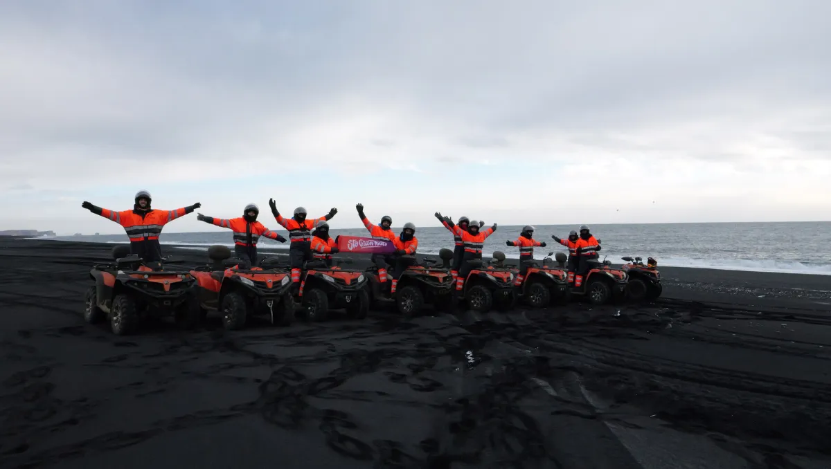 The group in orange overalls with arms wide open on their quads, lined up on a black sand beach