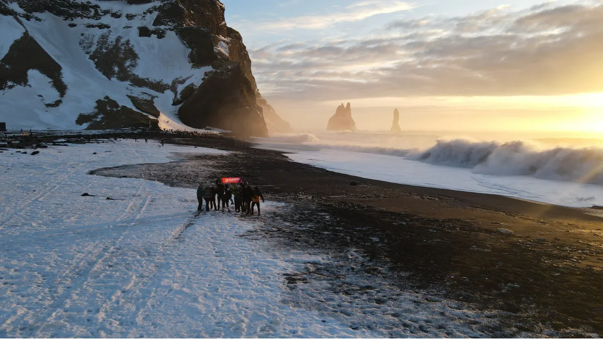 The group with the Sto Gran Tour banner on an Icelandic black beach, at sunset between snow and waves