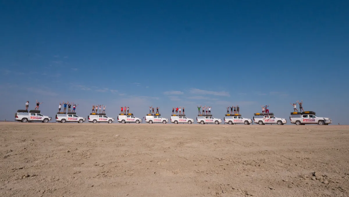 A row of Sto Gran Tour pickups on the salt flat, with travelers standing on the roofs with their arms raised